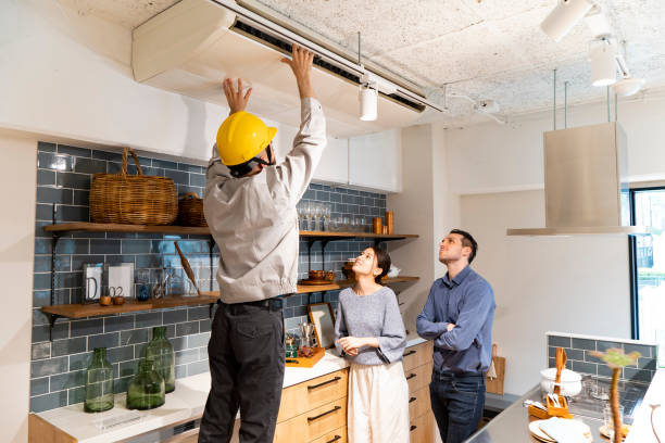 a repairman wearing a yellow helmet and checking the air conditioner