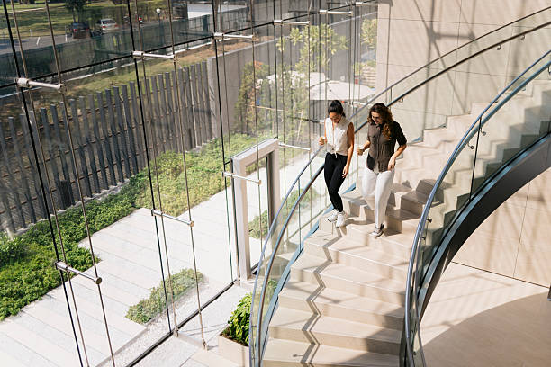 two businesswomen walking and talking on stairs in modern office building